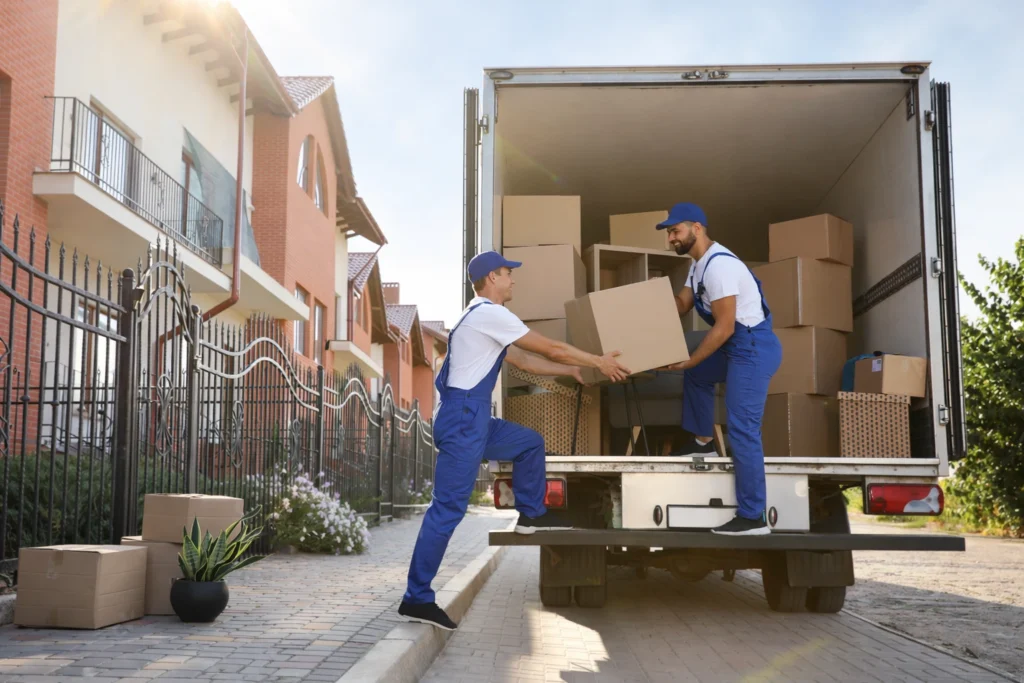 Umzugsunternehmen Mitarbeiter verladen Umzugskartons in LKW vor Wohnhaus